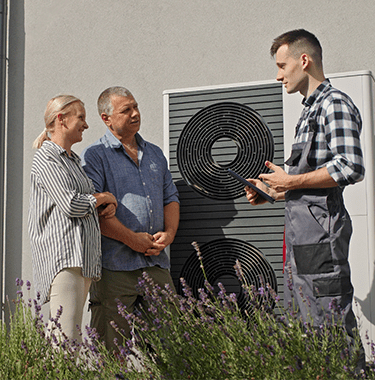 A mid shot of a couple and a man talking whilst stood outside in front of a heating system.